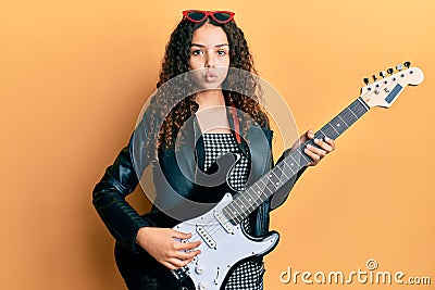 Teenager hispanic girl playing electric guitar looking at the camera blowing a kiss being lovely and sexy Stock Photo