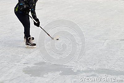 Teenager with hockey stick, wearing ice-skating, skates and drags the puck. Active sport outdoor Stock Photo