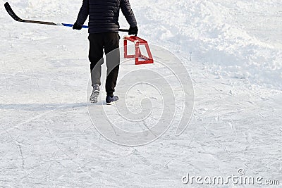 Teenager with hockey stick, wearing sneakers, goes to little training red goal on park ice rink. Active sport outdoor Stock Photo