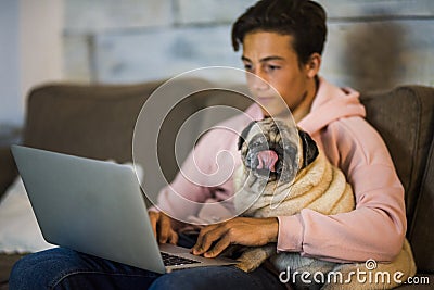 Teenager at home working with his laptop on the sofa with a pug next to him - best friends on the sofa hugged together Stock Photo