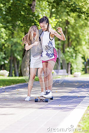 Teenager Lifestyle Ideas and Concepts. Two Teenage Girlfriends Having Fun Skating Longboard in Park Outdoors Stock Photo