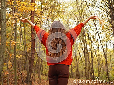 A teenager lifting her hands up with joy. A girl wearing orange sweater and brown jeans Stock Photo