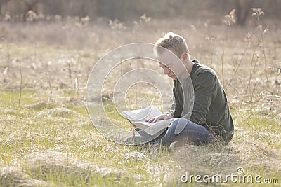 Teenager in open field reading Bible Stock Photo