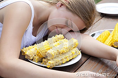 Girl eating lot boiled corn. Putting your head on the table Stock Photo