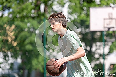 Teenager playing basketball smiling, cheerful. Fit boy with basketball ball outdoors. Kid dribbling the ball at the court Stock Photo