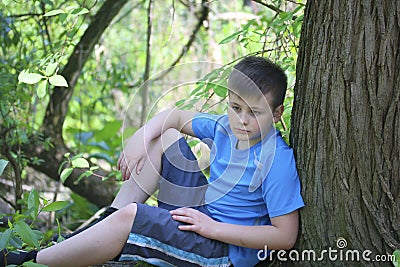 A teenager poses for a photographer while walking in the park. Sits, leaning on a tree. Stock Photo