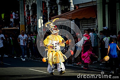 Teenager in scary yellow clown costume passes by city street at dominican carnival Editorial Stock Photo