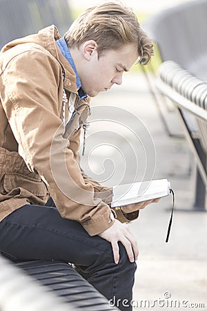 Teenager sitting on bench reading Bible Stock Photo