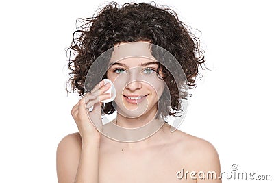 Teenager skincare. Beautiful teenage girl with gorgeous curly hair using cotton pad to remove make up, looking at camera smiling. Stock Photo