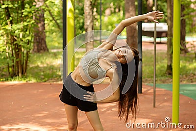 Teenager sports summer activities, the girl does sports exercises outdoor, the athlete does inclines in the street gym Stock Photo