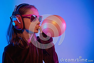 Teenager in sunglasses listening music with headphones in trendy neon light. Emotional portrait millennial pretty girl Stock Photo