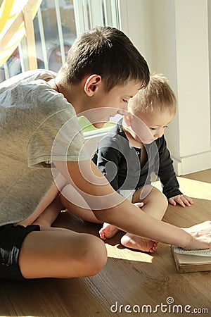 A teenager teaches his younger brother a toddler by showing a book. Stock Photo