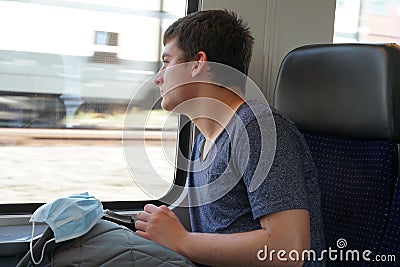 A teenager on train with his rucksack and facial mask prepared for use if needed Stock Photo