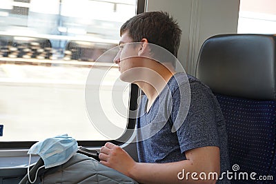 A teenager on train with his rucksack and facial mask prepared for use if needed Stock Photo