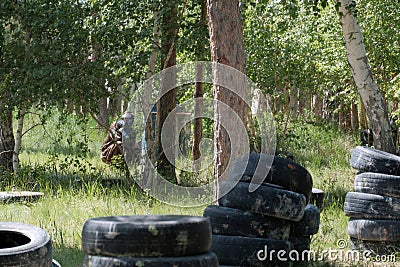 Landfill in the forest for a team game in paintball. A teenager wearing a black protective mask and camouflage clothes with arms i Editorial Stock Photo