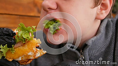 Teenagerjunge in schwarzen Gummihandschuhen essen einen Burger Köstliche, saftige frische Burger auf dem Tisch in Fastfood stock video footage Teenagerjunge in schwarzen Gummihandschuhen essen einen Burger Köstliche, saftige frische Burger auf dem Tisch in Fastfood stock video footage
