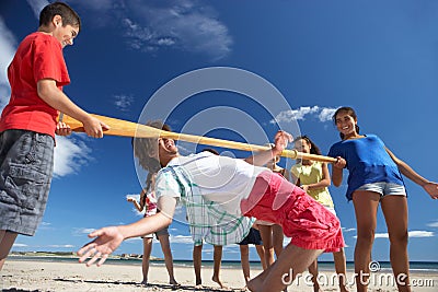 Teenagers doing limbo dance on beach Stock Photo