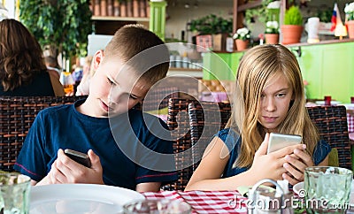 Teenagers having fun with mobile phones in cafe. Modern lifestyle and technology concept. Children sitting in restaurant and Stock Photo