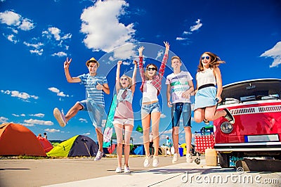 Teenagers at summer festival jumping by vintage red campervan Stock Photo