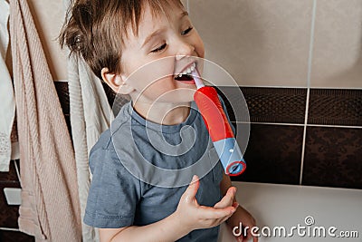 The naughty baby brushes his teeth with a brush at the washbasin and smiles and looks at himself towards the mirror. Portrait clos Stock Photo