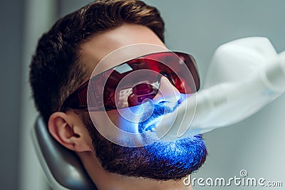 Teeth whitening. Man having teeth whitened by dental UV laser whitening device. Teeth whitening machine,eyes protected with Stock Photo