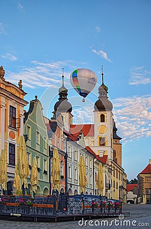 One hot air balloon flies over the main square of the city Telc and near two towers of Name of Jesus Church Kostel Jmena Jezis Editorial Stock Photo