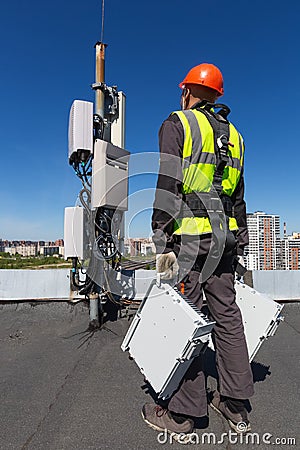 Telecommunication engineer in helmet and uniform holds telecomunication equipment in his hand and antennas of GSM DCS Stock Photo