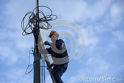 A telecoms worker is shown working from a utility pole ladder while wearing high visibility personal safety clothing, PPE, and a Stock Photo