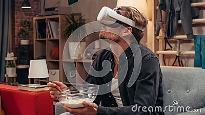 Television Sitcom Concept: Guy Using Virtual Reality Headset Eating Breakfast in Living Room. Funny Stock Photo