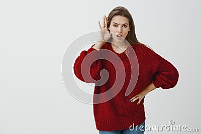 Tell me everything he said to you. Indoor shot of shocked and intense charming female coworker in loose red sweater Stock Photo