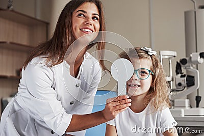 Tell me what you see on the board. Little girl tries new blue glasses in ophthalmologic office with female doctor Stock Photo