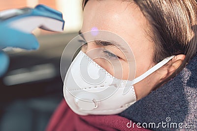 Temperature check point - the woman behind the wheel of the car in an anti-virus mask is subjected to temperature measurement Stock Photo