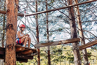 Ten-year-old girl in a helmet on a rope town outdoors in the summer. Rest before the passage of obstacles. To overcome fear Stock Photo