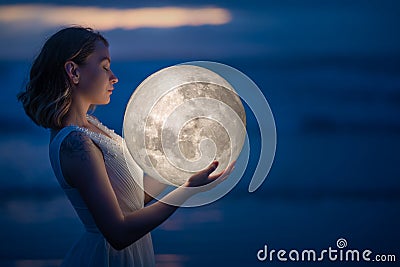 Tender image of a girl. Female magic. Beautiful attractive girl on a night beach with sand hugs the moon, art photo. On a dark Stock Photo