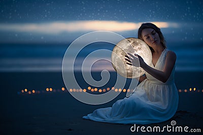 Tender image of a girl; female magic. Beautiful attractive girl on a night beach with sand and stars hugs the moon, art photo. On Stock Photo