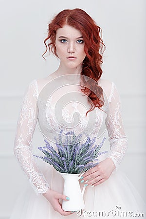 Tender retro portrait of a young beautiful dreamy redhead woman in beautiful white dress with bouquet of lavender. Stock Photo