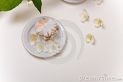 Tender sand tart with powdered sugar on plate with some jasmine flowers around on white table. Sweet pastry, spring blossom Stock Photo