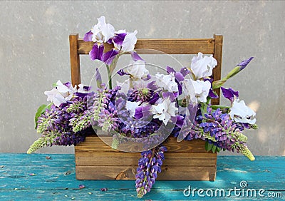 Tender white irises with purple lupins in a wooden crate. Beautiful exquisite bouquet on the green wooden table Stock Photo