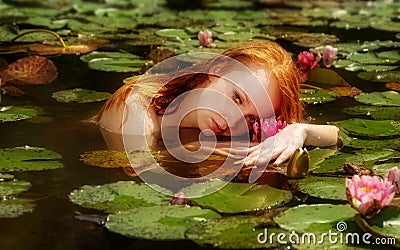 Tender young redhead woman Ophelia floats sensually seductively in the water, lake, pond, marsh and playing with waterlilies Stock Photo