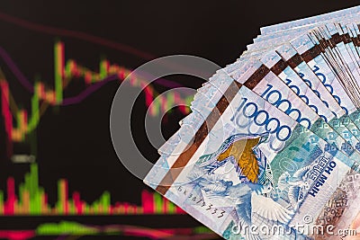 Tenge in Kazakhstan against the background of a laptop with an open chart of the currency market or stock exchange. Hands holding Stock Photo
