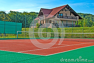 Tennis court, a beautiful chalet in the back and surrounded by trees and hills Stock Photo