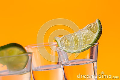 Tequila shot with a slice of lime on the glass orange background Stock Photo