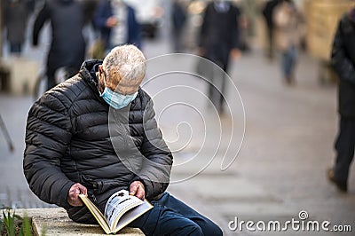 Man with medical mask reads a book outdoors Editorial Stock Photo
