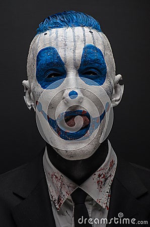 Terrible clown and Halloween theme: Crazy blue clown in black suit isolated on a dark background in the studio Stock Photo