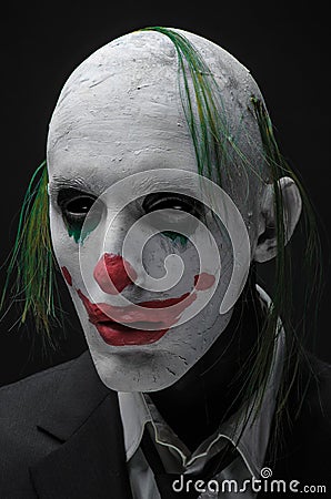 Terrible clown and Halloween theme: Crazy terrible green clown in black suit isolated on a dark background in the studio Stock Photo