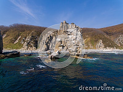 A huge stone in the form of an arch stands in the middle of the sea against the background of sheer cliffs. The territory of the Stock Photo