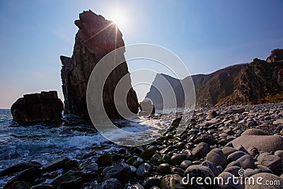 A huge stone in the form of an arch stands in the middle of the sea against the background of sheer cliffs. The territory of the Stock Photo
