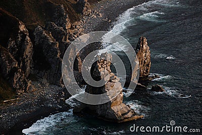 A huge stone in the form of an arch stands in the middle of the sea against the background of sheer cliffs. The territory of the Stock Photo