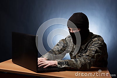 Terrorist working on his computer. Masked cyber terrorist hacking army intelligence Stock Photo