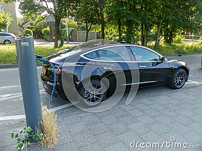 Tesla model electric car charging batteries at plug in charge station in leafy green suburb inthe Netherlands Editorial Stock Photo